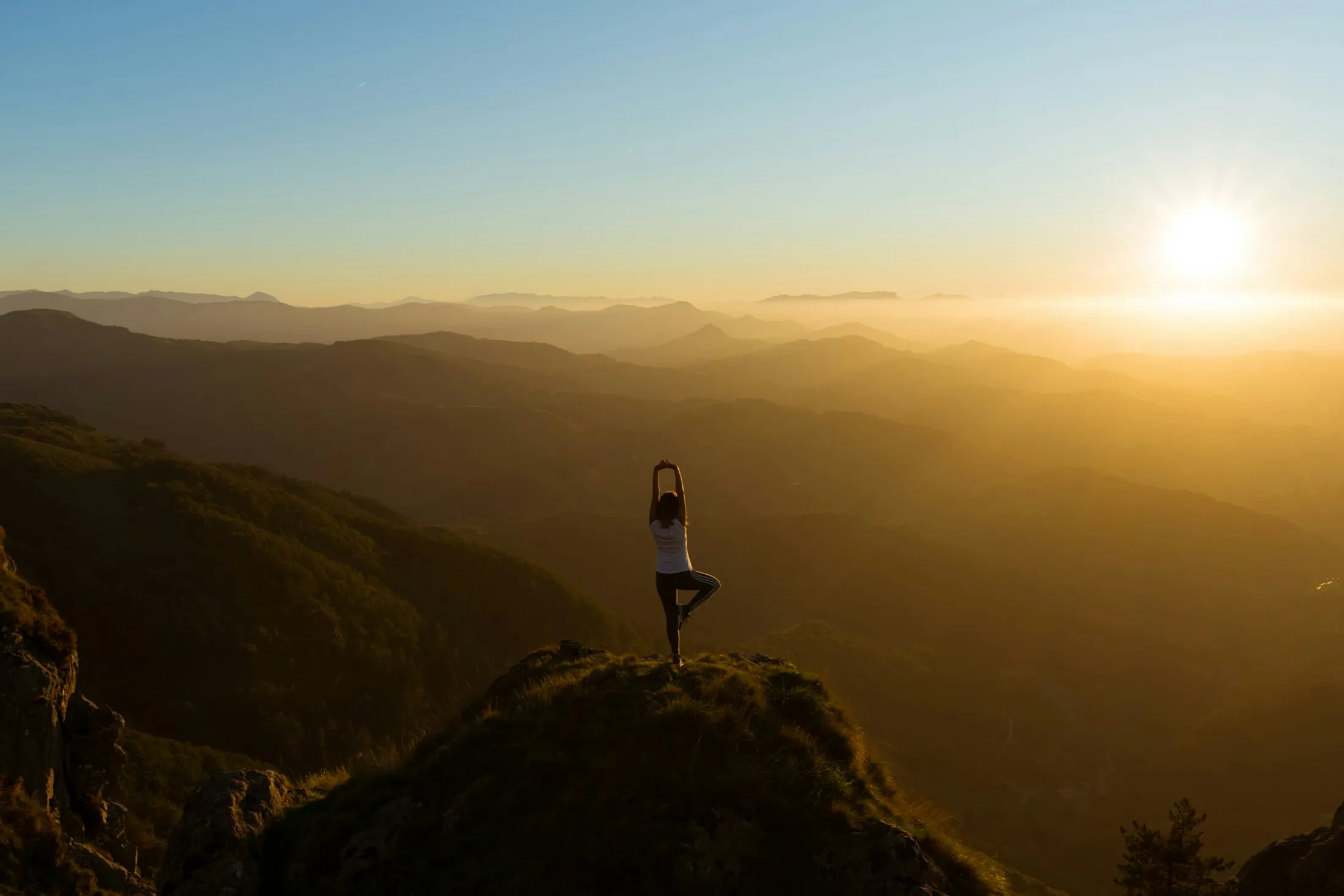 A woman in tree pose on a mountain ridge at sunrise